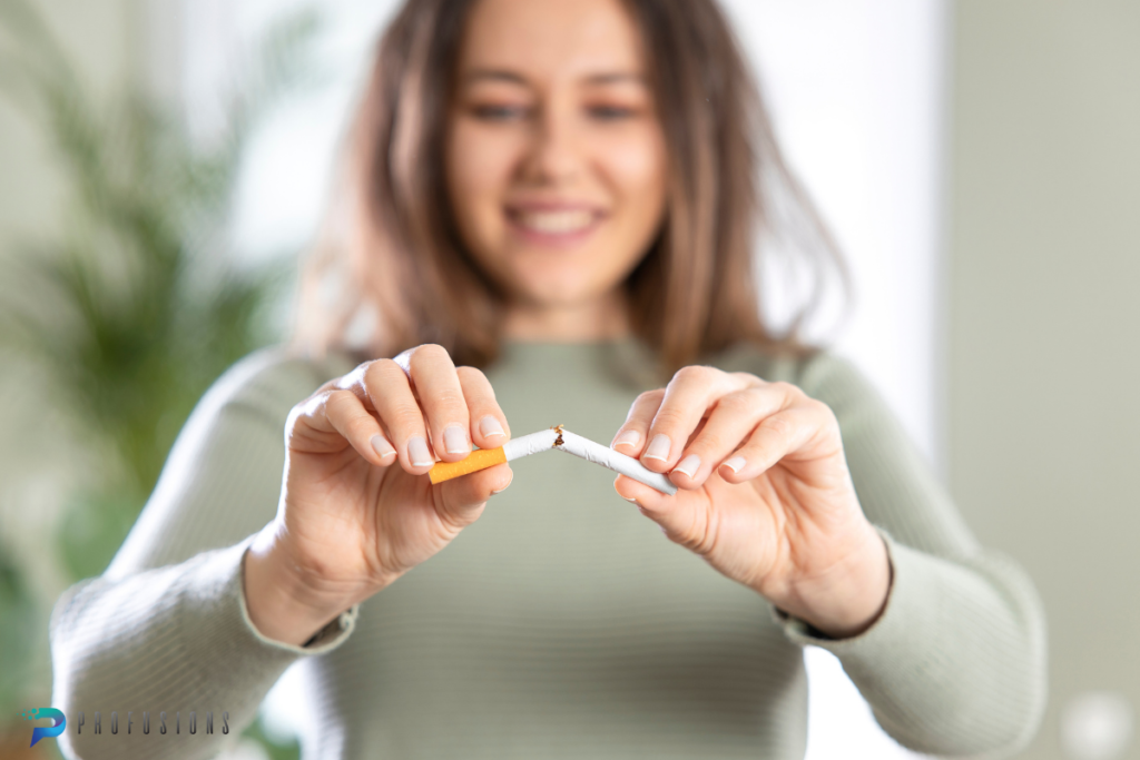 A close-up shot focuses on a woman's hands as she decisively snaps a cigarette in half. In the background, her face is softly blurred but she is clearly smiling, conveying a sense of empowerment and relief in the act of breaking addiction to smoking.